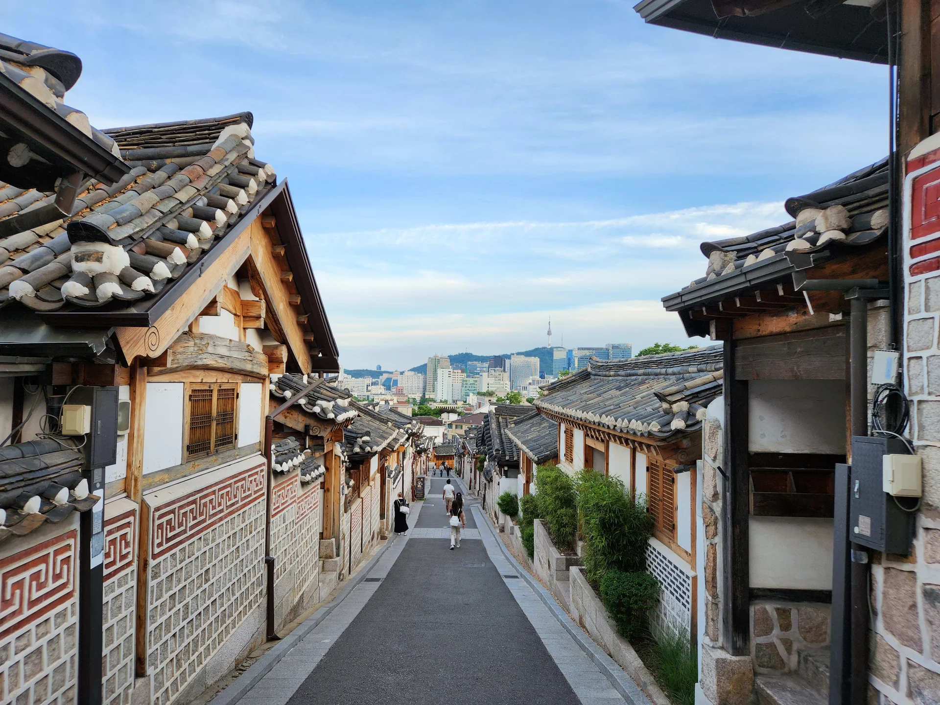 Experience the vibrant pulse of Korean city life through these dynamic street wallpapers. Bustling crosswalks in Myeongdong, colorful shop fronts in Hongdae, rain-slicked sidewalks reflecting neon signs, and everyday moments of commuters, street vendors, and cyclists moving through Seoul's urban rhythm — each image tells a story of a city constantly in motion.

Beyond Seoul, you'll find the charming streetscapes of Busan's hillside neighborhoods, the retro storefronts of Jeonju, and quiet residential lanes where laundry dries on balconies above parked scooters. These free Korean street wallpapers are perfect as an aesthetic phone background for anyone captivated by the raw energy and visual richness of Korean urban culture., 북촌로11나길, Gahoe-dong, Seoul — Free Korean aesthetic wallpaper
