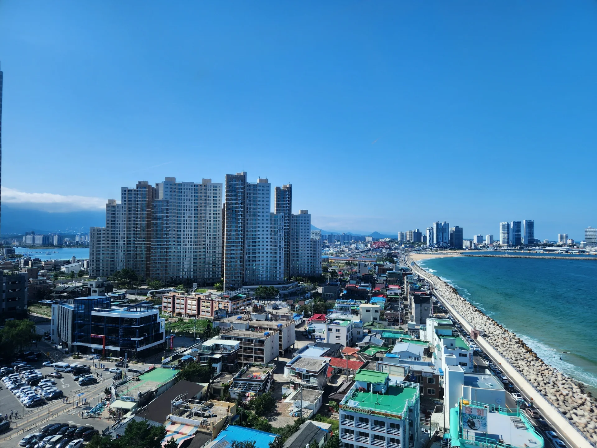 Experience the vibrant pulse of Korean city life through these dynamic street wallpapers. Bustling crosswalks in Myeongdong, colorful shop fronts in Hongdae, rain-slicked sidewalks reflecting neon signs, and everyday moments of commuters, street vendors, and cyclists moving through Seoul's urban rhythm — each image tells a story of a city constantly in motion.

Beyond Seoul, you'll find the charming streetscapes of Busan's hillside neighborhoods, the retro storefronts of Jeonju, and quiet residential lanes where laundry dries on balconies above parked scooters. These free Korean street wallpapers are perfect as an aesthetic phone background for anyone captivated by the raw energy and visual richness of Korean urban culture., Cheonghohaean-gil (Donghaean Bicycle Path), Cheongho-dong, Sokcho-si — Free Korean aesthetic wallpaper