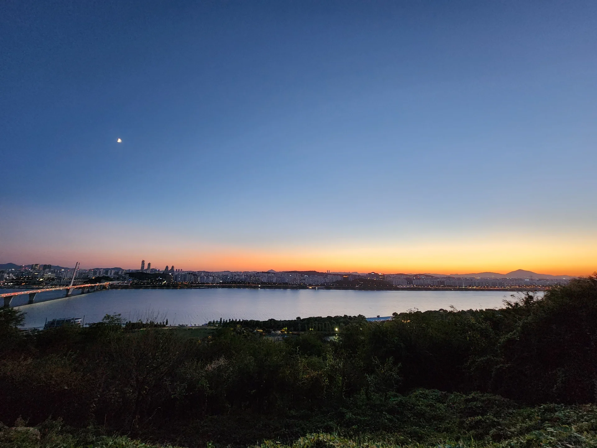 Light up your phone with the electric energy of Seoul after dark. These Korean nightscape wallpapers capture the city at its most cinematic — neon signage stacking up narrow alleyways, glowing street food stalls sending steam into cold night air, illuminated bridges spanning the Han River, and the shimmering towers of Gangnam reflected in rain-wet streets.

Seoul's nighttime personality is bold, colorful, and endlessly photogenic. You'll find the moody glow of Itaewon bars, the cyberpunk atmosphere of Euljiro's industrial blocks, and panoramic cityscapes from hilltop viewpoints where the city stretches to the horizon in every direction. Free download these aesthetic Seoul night wallpapers for a phone background that pulses with urban energy., Gangbyeonbuk-ro, Sangam-dong, Seoul — Free Korean aesthetic wallpaper