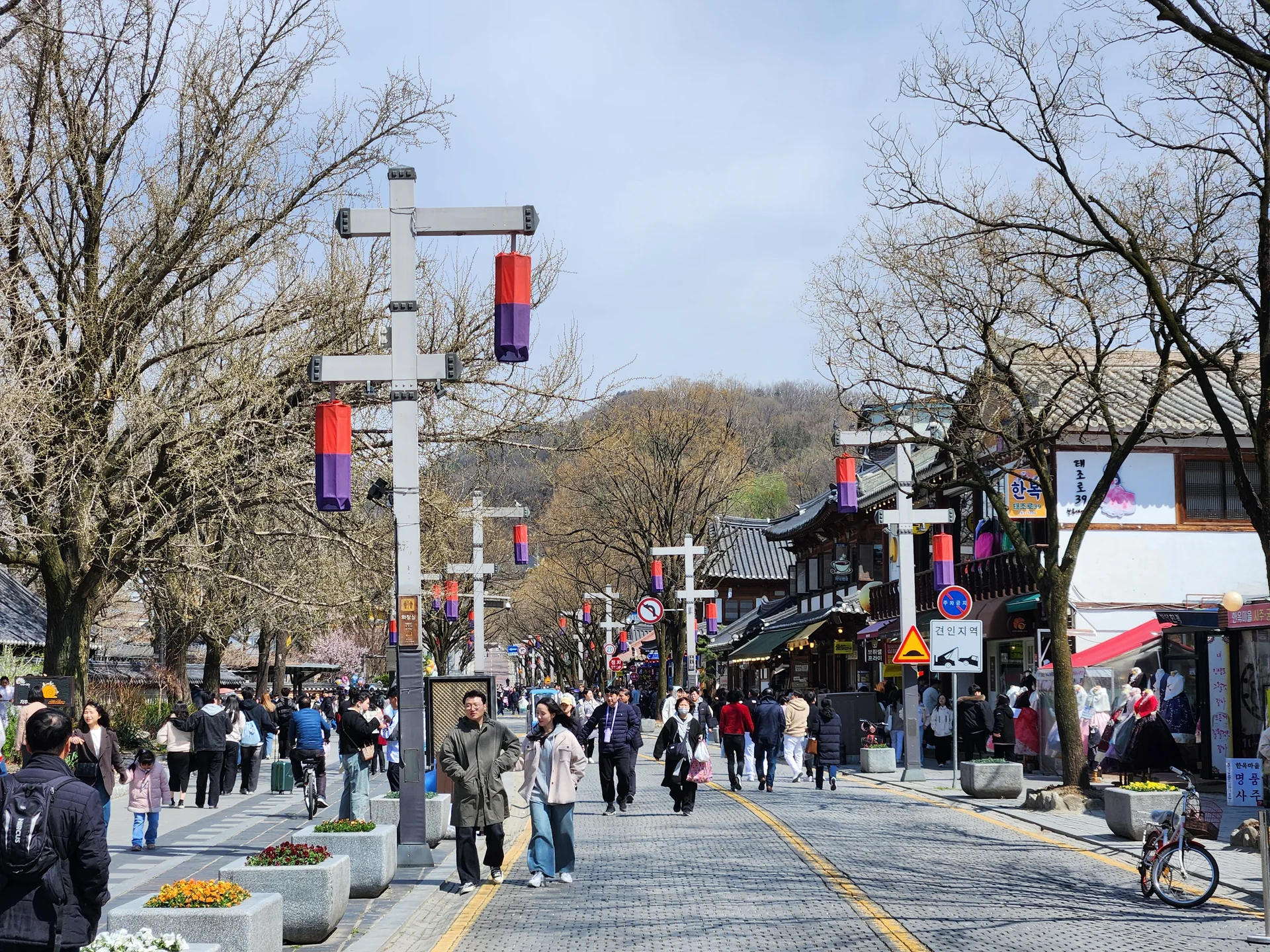 Experience the vibrant pulse of Korean city life through these dynamic street wallpapers. Bustling crosswalks in Myeongdong, colorful shop fronts in Hongdae, rain-slicked sidewalks reflecting neon signs, and everyday moments of commuters, street vendors, and cyclists moving through Seoul's urban rhythm — each image tells a story of a city constantly in motion.

Beyond Seoul, you'll find the charming streetscapes of Busan's hillside neighborhoods, the retro storefronts of Jeonju, and quiet residential lanes where laundry dries on balconies above parked scooters. These free Korean street wallpapers are perfect as an aesthetic phone background for anyone captivated by the raw energy and visual richness of Korean urban culture., Taejo-ro, Jeon-dong, Jeonju-si — Free Korean aesthetic wallpaper