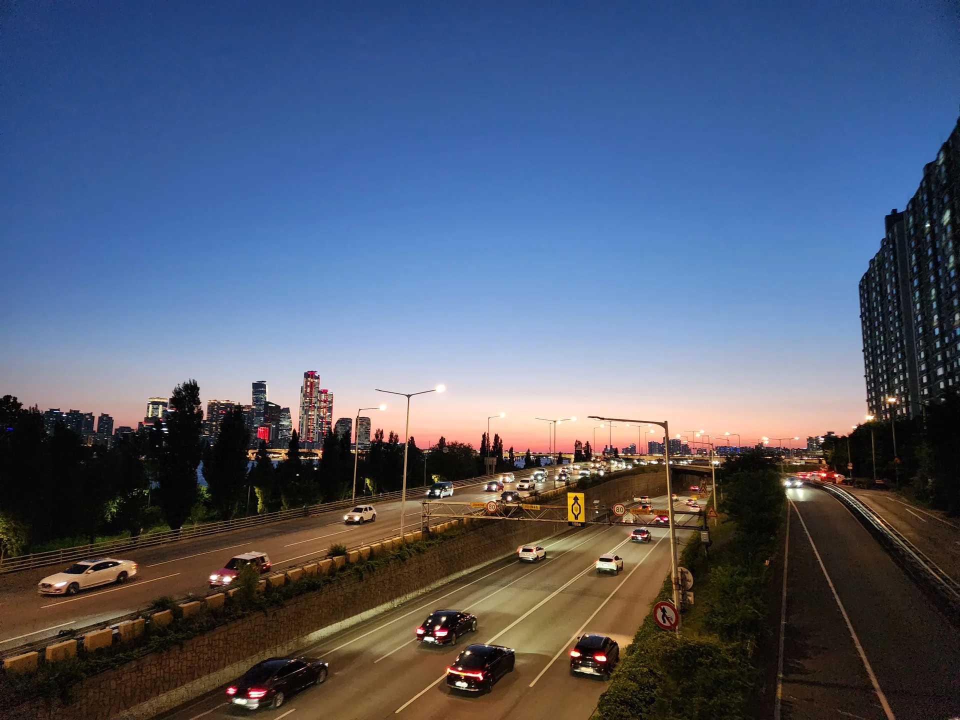 Experience the vibrant pulse of Korean city life through these dynamic street wallpapers. Bustling crosswalks in Myeongdong, colorful shop fronts in Hongdae, rain-slicked sidewalks reflecting neon signs, and everyday moments of commuters, street vendors, and cyclists moving through Seoul's urban rhythm — each image tells a story of a city constantly in motion.

Beyond Seoul, you'll find the charming streetscapes of Busan's hillside neighborhoods, the retro storefronts of Jeonju, and quiet residential lanes where laundry dries on balconies above parked scooters. These free Korean street wallpapers are perfect as an aesthetic phone background for anyone captivated by the raw energy and visual richness of Korean urban culture., Ichon-ro, Ichon 2(i)-dong, Seoul — Free Korean aesthetic wallpaper