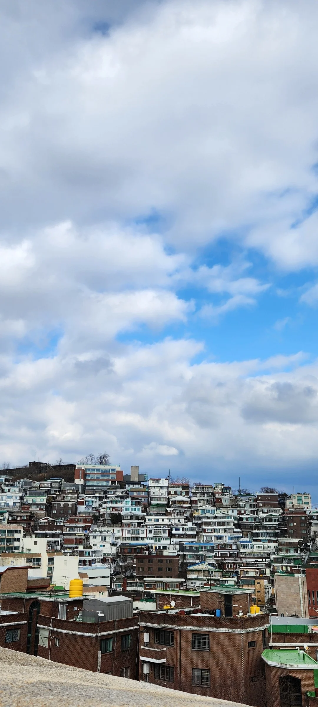 Experience the vibrant pulse of Korean city life through these dynamic street wallpapers. Bustling crosswalks in Myeongdong, colorful shop fronts in Hongdae, rain-slicked sidewalks reflecting neon signs, and everyday moments of commuters, street vendors, and cyclists moving through Seoul's urban rhythm — each image tells a story of a city constantly in motion.

Beyond Seoul, you'll find the charming streetscapes of Busan's hillside neighborhoods, the retro storefronts of Jeonju, and quiet residential lanes where laundry dries on balconies above parked scooters. These free Korean street wallpapers are perfect as an aesthetic phone background for anyone captivated by the raw energy and visual richness of Korean urban culture., Changsin 11-gil, Changsin 2(i)-dong, Seoul — Free Korean aesthetic wallpaper